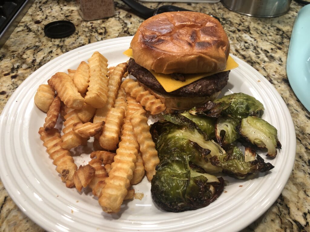 cheese burger topped with grilled onions and avocado, and served with french fries and brussell sprouts